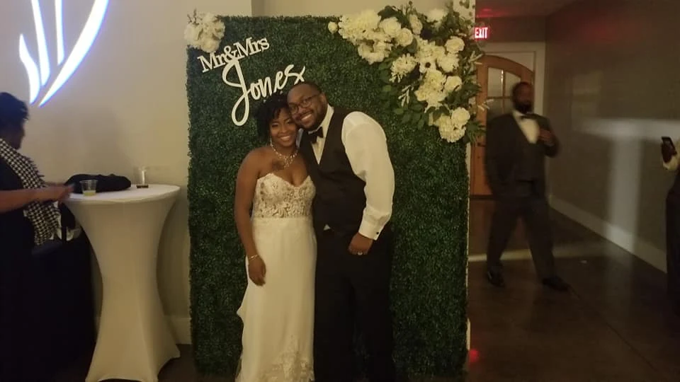 A wedding couple in front of a floral reception backdrop