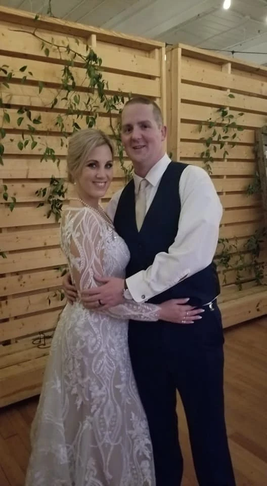 A wedding couple posing at a wooden reception backdrop
